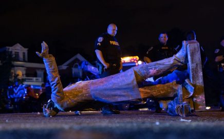 Two police officers stand behind a toppled confederate statue.