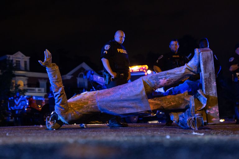 Two police officers stand behind a toppled confederate statue.
