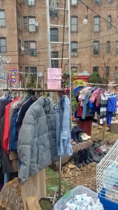 clothing racks in the garden full of shirts and coats, with a sign that reads "Free Store!"